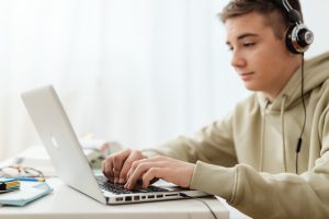 Oppimisen apuvälineet -sivun kuvituskuvassa nuori mies tietokoneella ja kuulokkeet